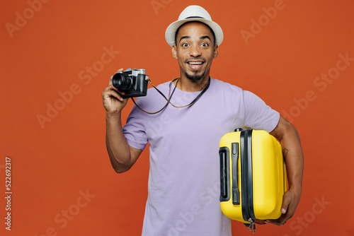 Traveler black man wear purple t-shirt hat hold suitcase photo camera isolated on plain orange color background. Tourist travel abroad on weekends spare time getaway. Air flight trip journey concept, #522692317