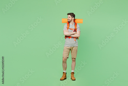 Full body fun smiling young traveler white man carry backpack stuff mat walk look aside on area isolated on plain green background. Tourist leads active lifestyle Hiking trek rest travel trip concept. © ViDi Studio