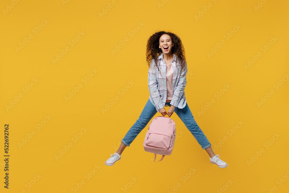 Full body young smiling happy black teen girl student she wear casual clothes hold backpack bag jump high look camera isolated on plain yellow color background. High school university college concept. Full body young smiling happy black teen girl student she wear casual clothes hold backpack bag jump high look camera isolated on plain yellow color background. High school university college concept.
