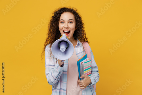 Young black teen girl student she wear casual clothes backpack bag hold books scream in megaphone discounts sale Hurry up isolated on plain yellow background. High school university college concept.