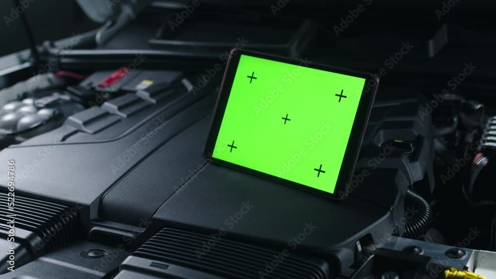 Unrecognizable male car service worker checking car and doing maintenance using a digital tablet computer with green screen chromakey, while standing near the opened bonnet