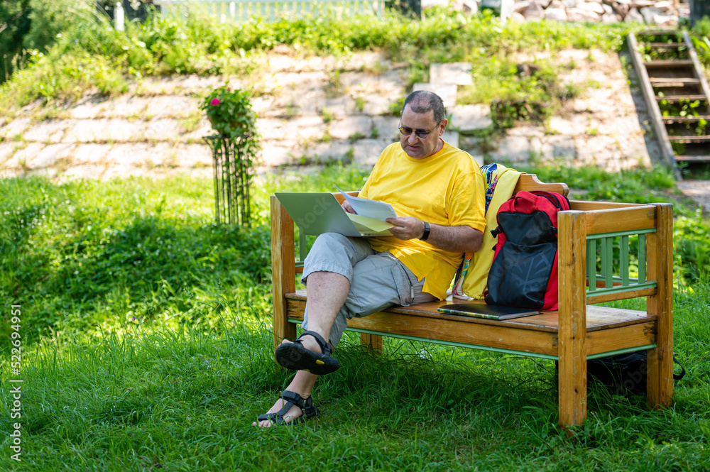 Fototapeta premium middle aged man with laptop and documents working outside in garden, green home office concept.
