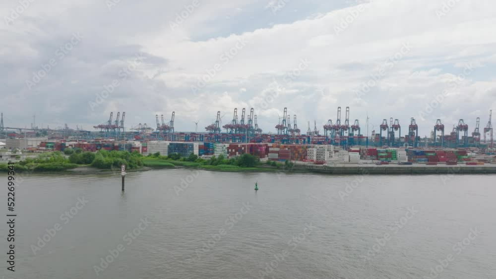 Forwards fly above water surface. Staked overseas containers in port. High harbour cranes in background. Global logistics and transportation. Hamburg, Germany
