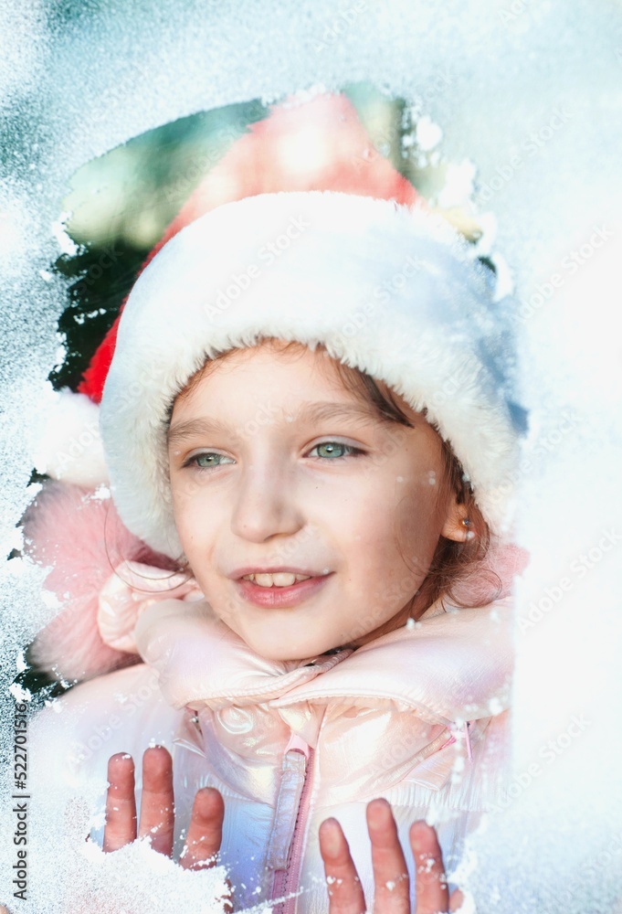 girl in santa claus costume looking throught the snowy window girl in santa claus costume looking throught the snowy window