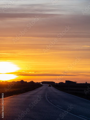 Beautiful sunset over paved road with two cars in the distance