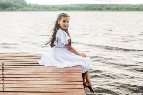 A little girl sits on a pier near the city lake outdoors. summer vacation