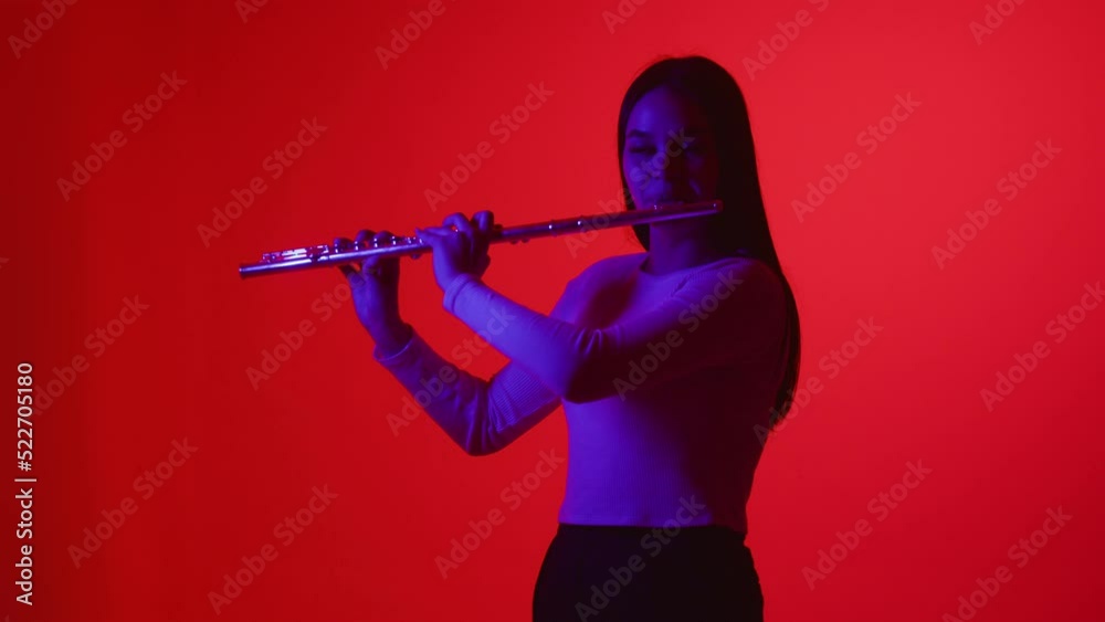Smooth flute playing on colored background. Girl in a white blouse plays wind instrument flute on a pink-purple background Smooth flute playing on colored background. Girl in a white blouse plays wind instrument flute on a pink-purple background