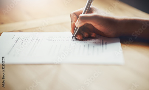 Closeup of business hands of a person filling out paperwork. Hand of an individual writing test, information or survey on paper to complete application or contract form on the desk at work. photo