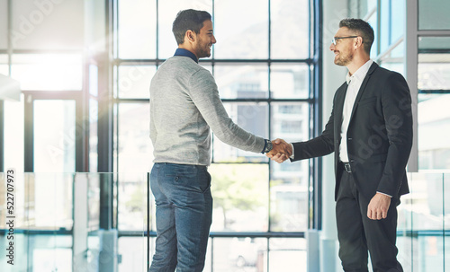 Businessman standing, smiling and with a handshake, greets a colleague in an office. Executive meets client or partner and shakes hands. Two happy professionals agree on a successful business project