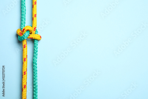 Top view of colorful ropes tied with knot on light blue background, space for text. Unity concept