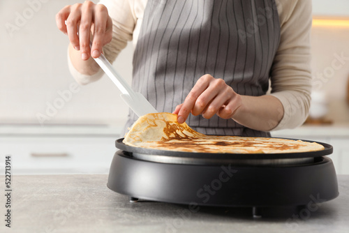 Woman cooking delicious crepe on electric pancake maker in kitchen, closeup