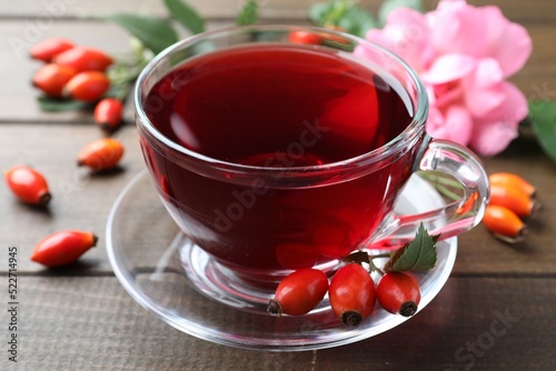 Aromatic rose hip tea and fresh berries on wooden table, closeup