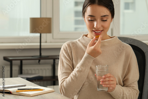 Fototapete Young woman with glass of water taking dietary supplement pill indoors, space fo