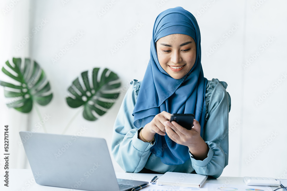Muslim business woman working on laptop computer and smartphone.
