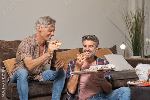 Fotografie, Obraz Positive mature male friends in casual clothes eating delicious pizza and drinki