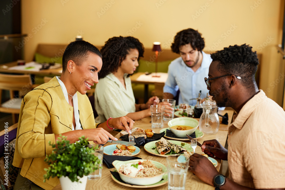 A multiracial group of friends sits at the dinner table in a restaurant and enjoys dinner.