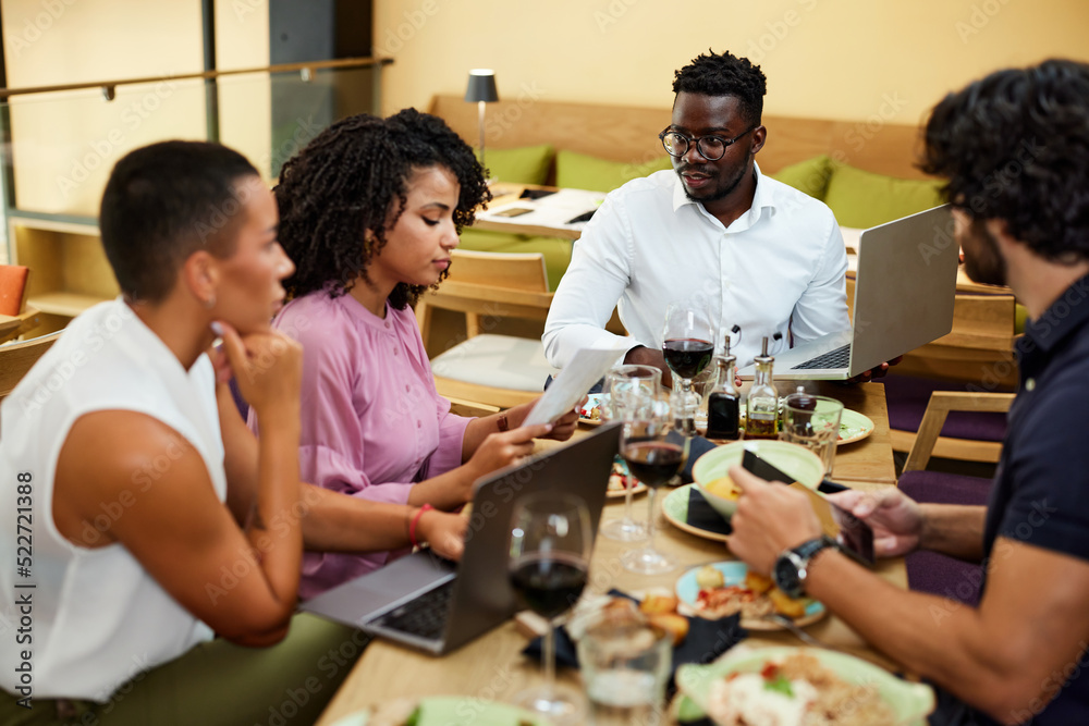 Multicultural colleagues sit in a restaurant at business lunch while listening to their boss explaining the project. Multicultural colleagues sit in a restaurant at business lunch while listening to their boss explaining the project.