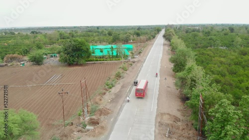 A moving drone aerial shot of vehicles passing on a straight road or highway surrounded by trees and farms in a rural area, Hampi, India  photo