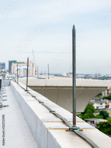 A lightning protection system is installed on the roof of a high-rise building as a bolt of conductor lightning to the ground, ground rod on the sky background..