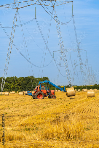 Straw bales on universal forks mounted on a Belarus or Petushok tractor. Collection of hay bales in one place for transportation. Rolls with straw under VL-750. Smolenskaya, Russia - July 16, 2022 photo