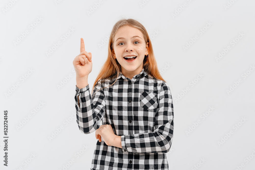 Portrait of smiling teen girl, pointing finger up, showing one, demonstrating banner, standing over white background in casual shirt Portrait of smiling teen girl, pointing finger up, showing one, demonstrating banner, standing over white background in casual shirt