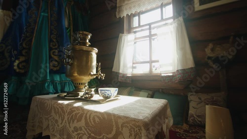 Cozy interior of a rustic wooden house with a samovar on a table in bright sunlight from a window with white curtains photo