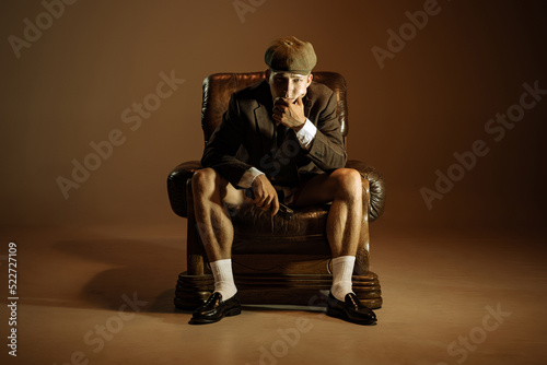 Cinematic portrait of young man, retro 1920s style english gangster wearing suit and cap isolated over dark vintage background. Business, family, art, fashion © master1305