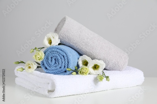 Clean soft towels with flowers on white table against light grey background