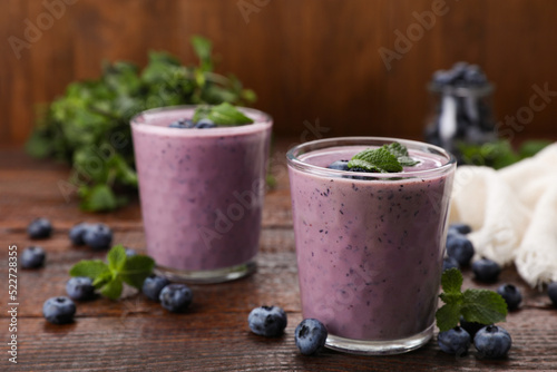 Glasses of blueberry smoothie with fresh berries and mint on wooden table, space for text