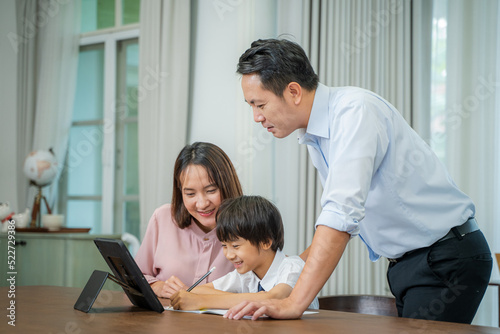 Little boy taking online class with parents helping him at home,Boy is writing in his book.