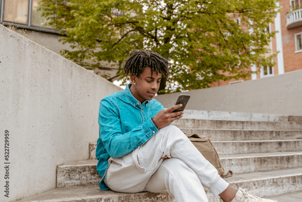 Fototapeta premium Dark-skinned man looking at smartphone sitting on steps