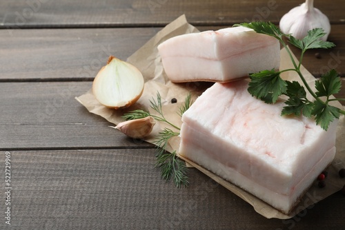 Tasty salt pork with herbs, onion and garlic on wooden table, space for text
