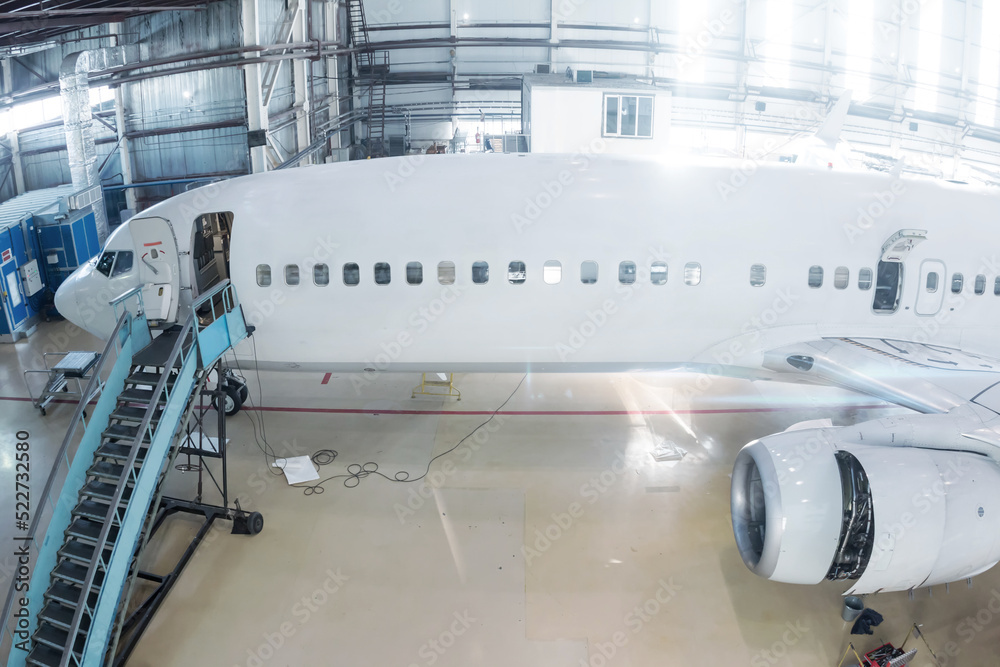 Fototapeta premium White passenger jetliner in the hangar. Airliner under maintenance. Checking mechanical systems for flight operations
