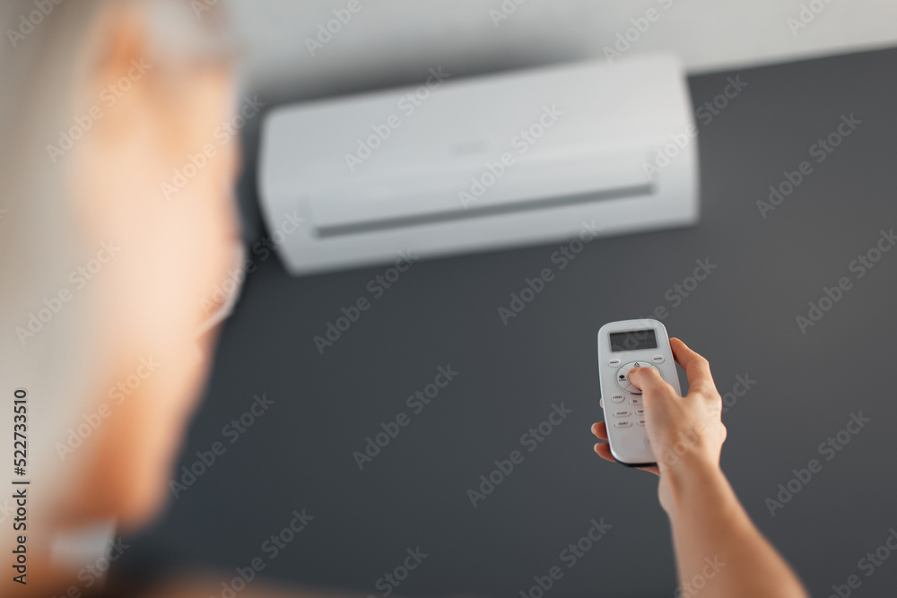 Fototapeta premium Young blonde female holds remote control of the air conditioner.