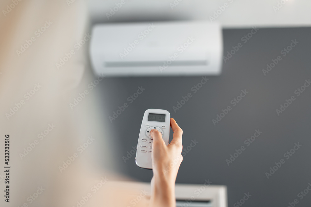 Young blonde female holds remote control of the air conditioner. Young blonde female holds remote control of the air conditioner.