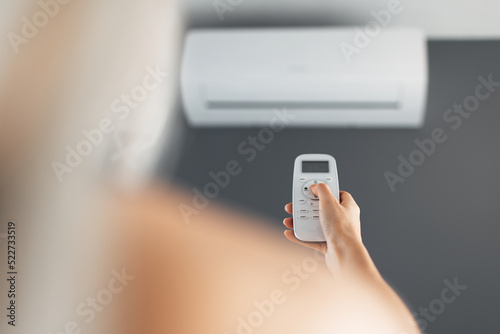Young blonde female holds remote control of the air conditioner.