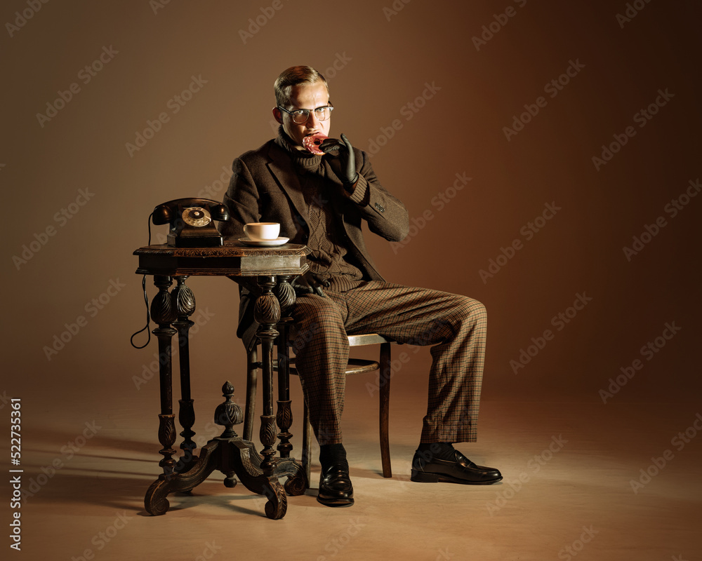 Retro style portrait of young man, writer and traveler wearing vintage style clothes isolated over dark brown background. Business, art, fashion concept