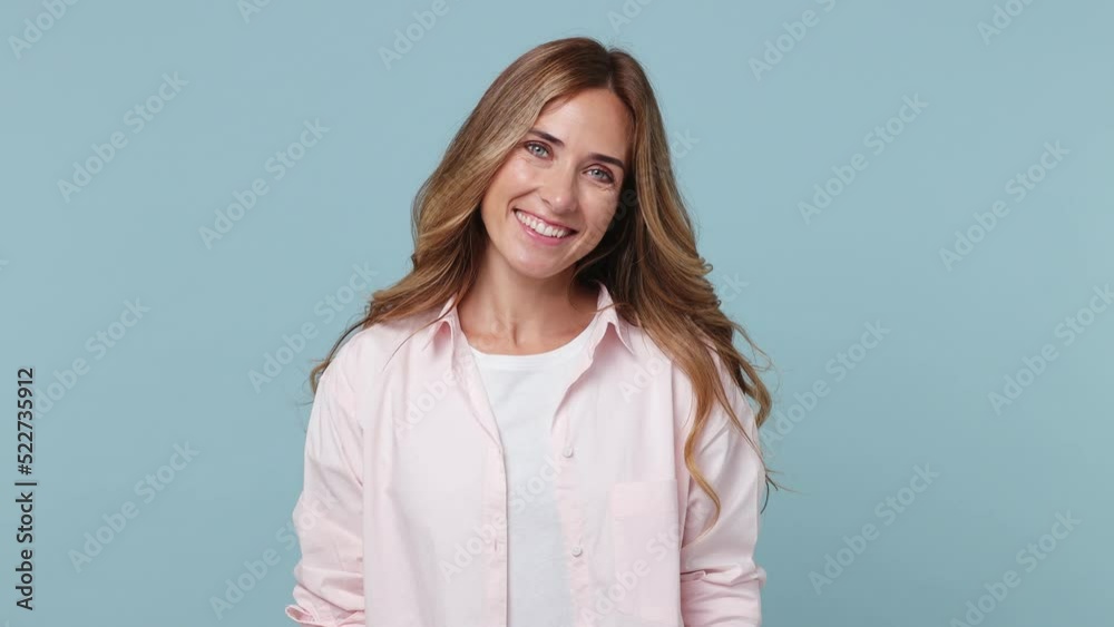 Young smiling charming happy fun confident caucasian woman 30s wear pink shirt looking camera wink eye blink isolated on plain pastel light blue cyan color background studio. People lifestyle concept