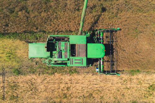 Top aerial view of a green agricultural combine with a revolving reel harvesting crop in a large grain field. . High quality photo photo