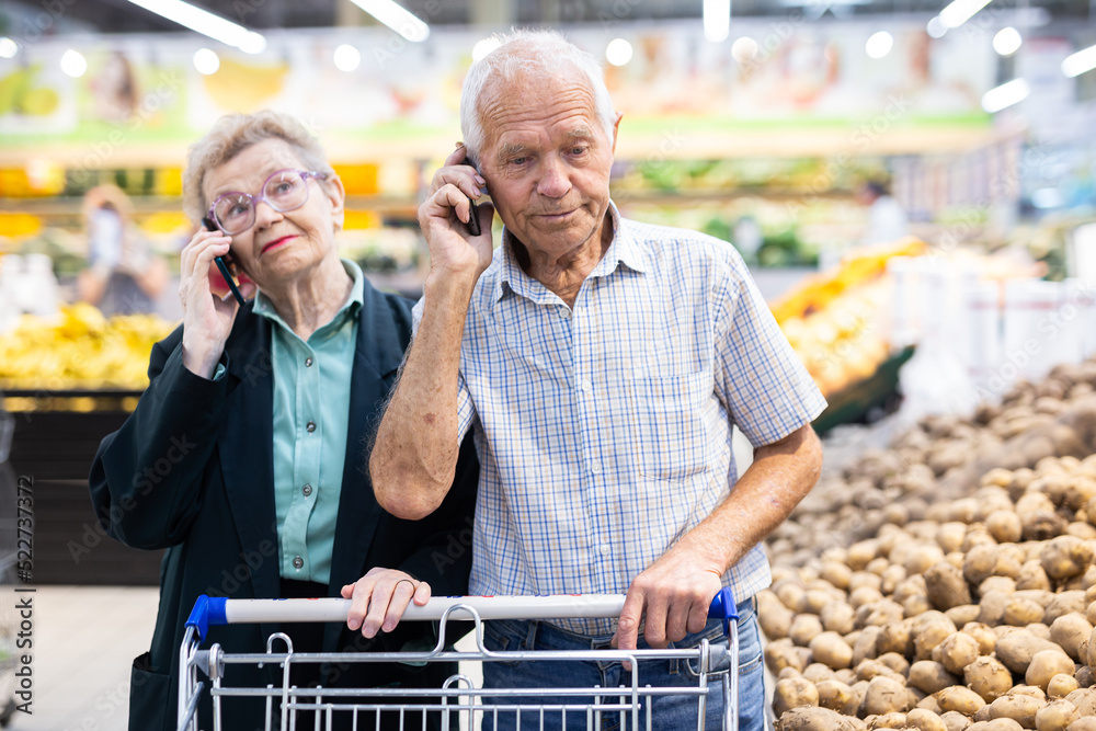mature european spouses talking on the phone in supermarket