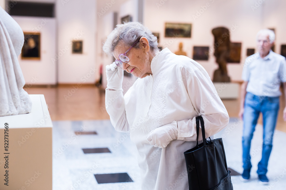 Obraz premium mature woman examines sculpture in an exhibition in hall of an art museum
