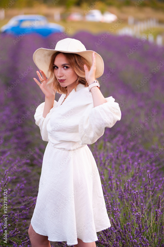 Young woman in a white dress and straw hat running in a lavender field 