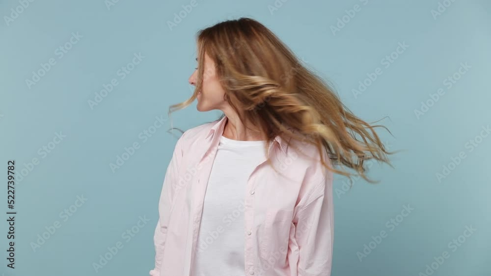 Slow motion fun fancy vivid young woman 30s wearing pink shirt looking camera charming smile play with curly hair isolated on plain pastel light blue cyan background studio. People lifestyle concept Slow motion fun fancy vivid young woman 30s wearing pink shirt looking camera charming smile play with curly hair isolated on plain pastel light blue cyan background studio. People lifestyle concept
