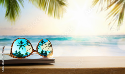 Art Computer and sunglasses on a wooden table. against the backdrop of sunset, the sun over a warm tropical beach photo