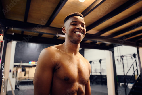 Happy African American male looking to the camera. Topless mixed race male exercising indoors in the gym with skipping rope. High quality photo