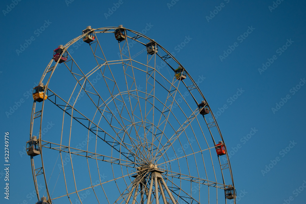 Ferris wheel without people in the clear blue sky. Ferris wheel in the park in bright sunlight during the day. Large white circular construction. Rides and attractions for children