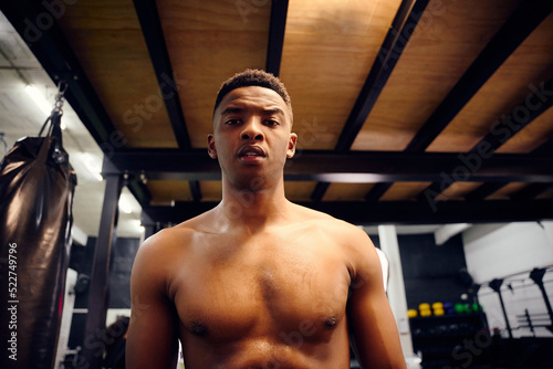 African American male looking serious to the camera. Topless mixed race male exercising indoors in the gym with skipping rope. High quality photo