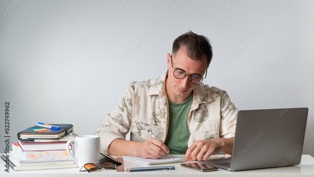 A student at a table with textbooks and notebooks writes in a notebook A student at a table with textbooks and notebooks writes in a notebook