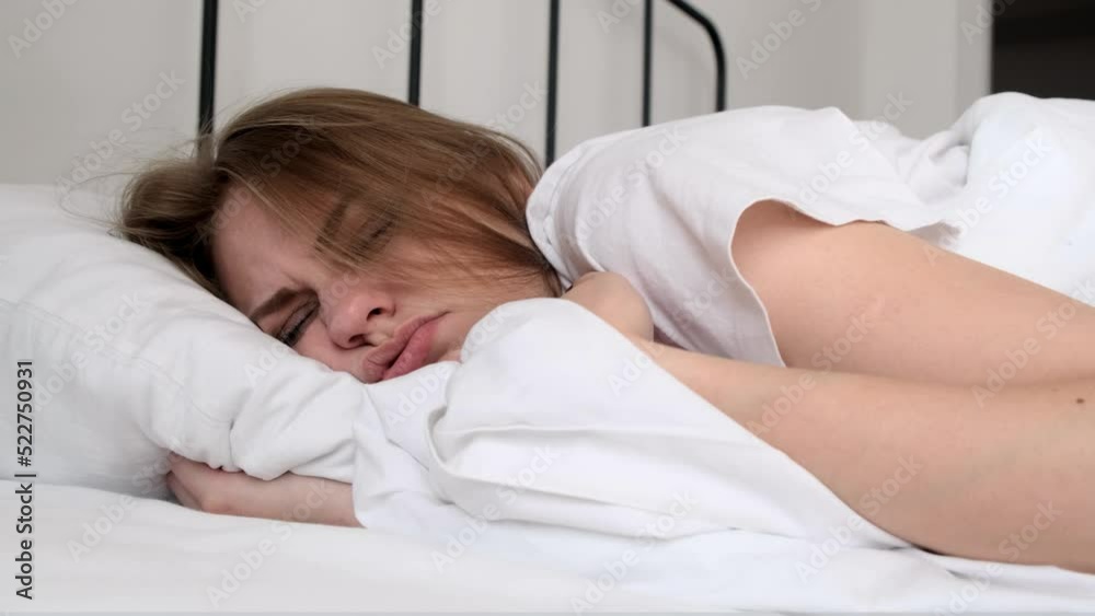 Hangover. Close-up the grimacing face of a sleeping young woman the morning after drinking alcohol. The girl feels bad and experiences discomfort. Headache, nausea and signs of alcohol poisoning Hangover. Close-up the grimacing face of a sleeping young woman the morning after drinking alcohol. The girl feels bad and experiences discomfort. Headache, nausea and signs of alcohol poisoning
