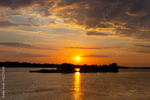 Sunset over the river and the reflection of the light of the Sun on the water, beautiful clouds over the forest in the distance. Dnieper river in Ukraine © Vlad Kazhan